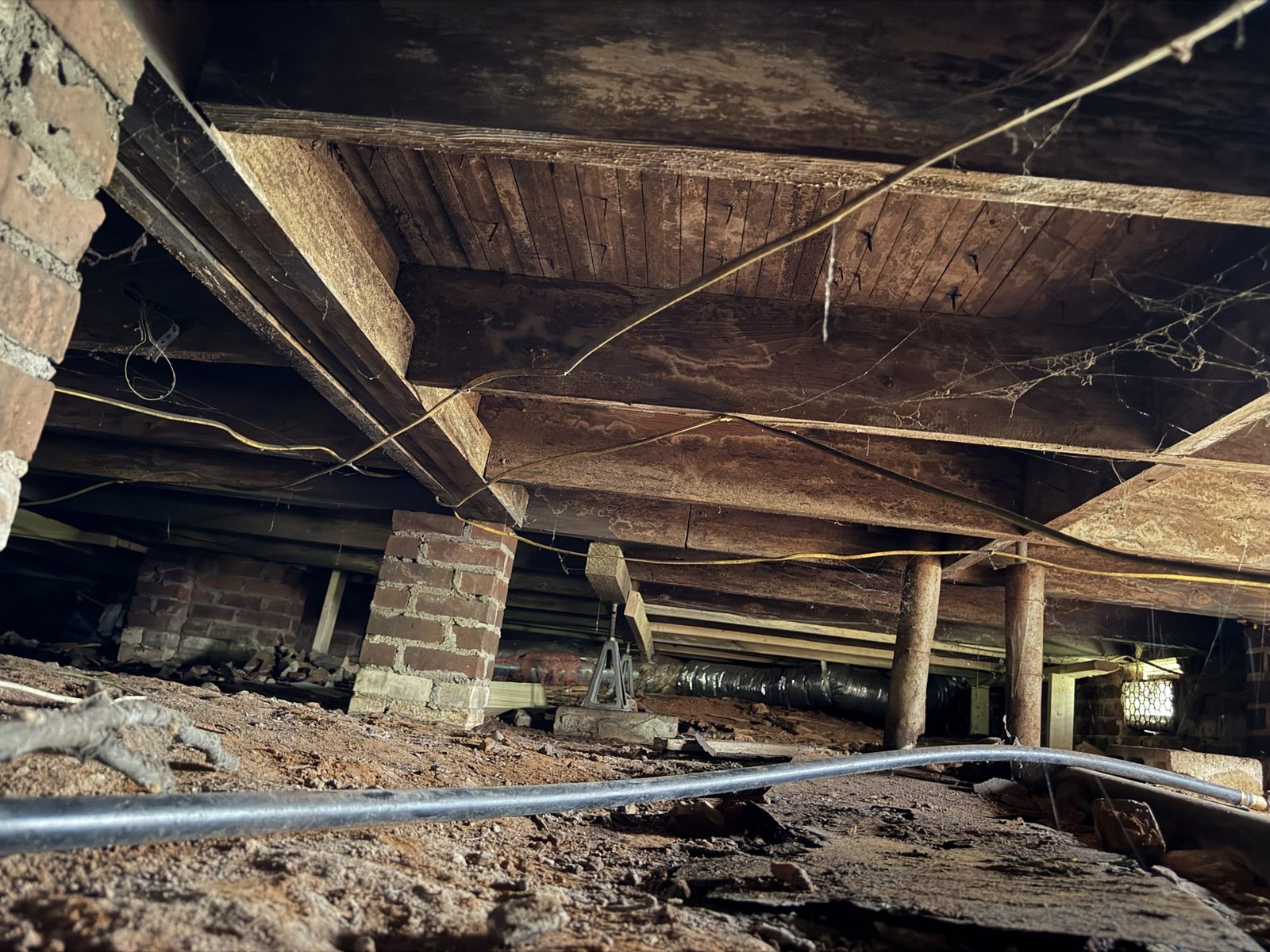 Crawlspace under a Greenville SC home with bare soil, wood joists and brick piers before encapsulation